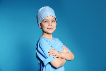 Cute little child in doctor uniform on color background