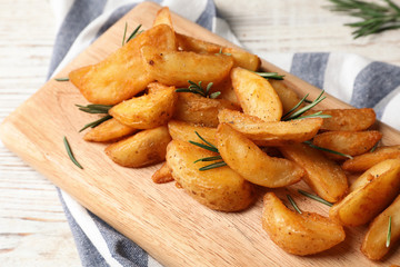 Wooden board with baked potatoes and rosemary on table, closeup