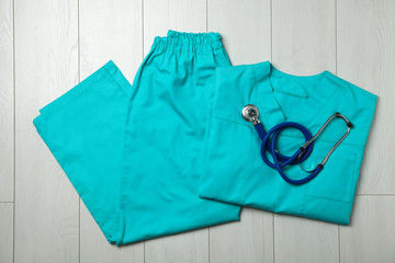 Clean scrubs and stethoscope on wooden background, top view. Medical objects