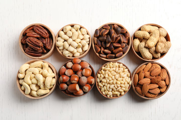 Bowls with different organic nuts on white wooden background, top view. Snack mix