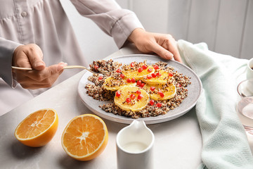 Obraz na płótnie Canvas Woman eating quinoa porridge with orange and pomegranate seeds at table, closeup