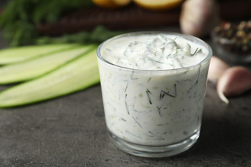 Cucumber sauce in glass bowl with ingredients on table, space for text. Traditional tzatziki