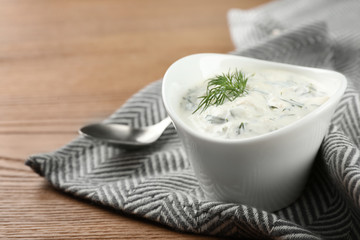 Cucumber sauce with spoon on wooden background, space for text. Traditional Tzatziki