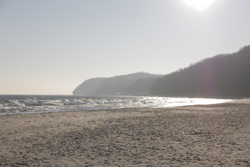 Baltic Sea coast during winter. A frosty, nice day. The reflection of the sun on the surface of the water. Strong wind, big waves. A wide, sandy beach. Hills overgrown with forest in the background.