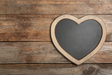 Heart shaped chalkboard on wooden background, top view with space for text