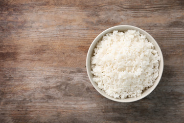 Fototapeta na wymiar Bowl of boiled rice on wooden background, top view with space for text
