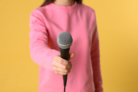 Young woman holding microphone on color background, closeup view
