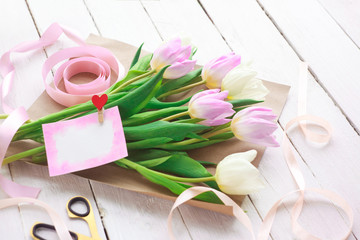 International Women's Day. A bouquet of white and pink tulips with a ribbon on a white background. Greeting card. Spring. Selective focus.