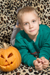 The young bright-haired boy is interested in a carved pumpkin on a halloween