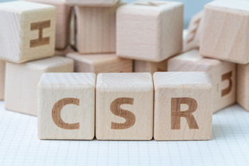 CSR, Corporate Social Responsibility concept, wooden cube block with letters forming acronym CSR on white gridline notebook, activity that company help people and community