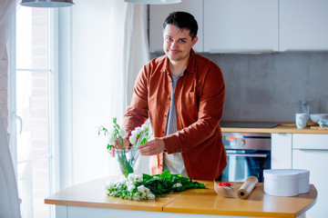 Young man wrapping wite roses on a table at kitchen