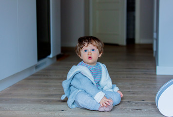 Naklejka premium Little baby sitting on a floor at home at kitche