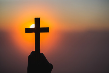 Silhouette off hands holding wooden cross  on sunrise background, Crucifix, Symbol of Faith.