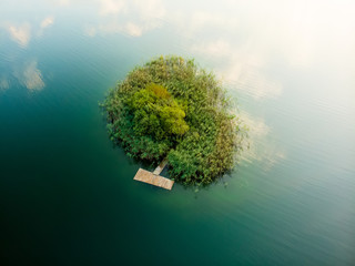 Aerial top down view of small island. Birds eye view of beautiful green waters of lake Gela surrounded by pine forests.