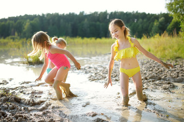 Three young sisters taking healing mud baths on lake Gela near Vilnius, Lithuania. Children having fun with mud.