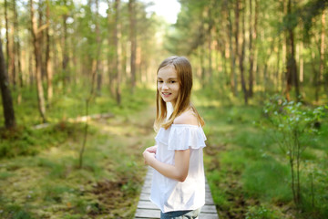 Naklejka na ściany i meble Cute young girl having fun during forest hike on beautiful summer day. Active family leisure.