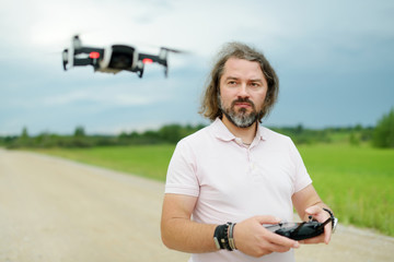 Man watching and navigating a drone. Man operating the drone by remote control. Drone hovering in...