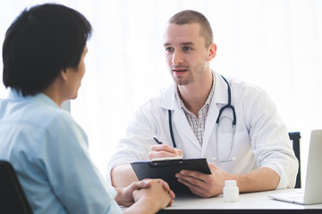 Doctor listening patient explain his symptom and notes to medical record.