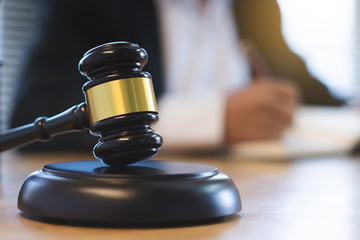 Close up view of auction hammer on the desk in lawyer office and lawyer writing document as background.