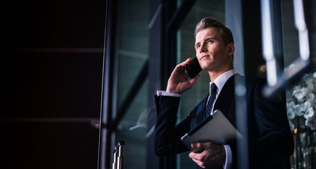 smart caucasian businessman black suit hand hold speaking smartphone walk pass glass entrance door