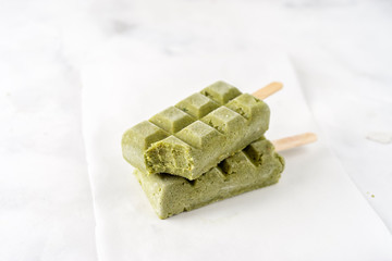 Two green vegan sorbet popsicles on white background
