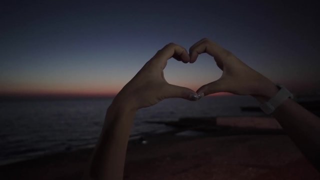 140) Girl makes a heart sign by her hands. Romantic evening on the seaside. Falling in love with sunset. Romantic vacation on the seaside.