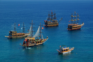 Tourist sailboats in turquoise waters of the Mediterranean sea beside the Turkish ancient fortress Alanya. Antalya, Turkey.