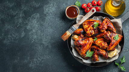 Baked chicken wings in barbecue sauce with sesame seeds and parsley in a cast iron pan on a dark...