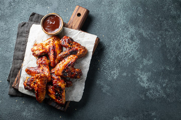 Roasted chicken wings in barbecue sauce with sesame seeds and parsley on a wooden board on a concrete table. Top view with copy space. Tasty snack for beer on a dark background. Flat lay