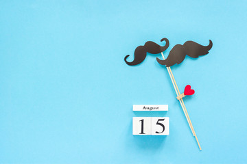 Couple paper mustache props fastened clothespin heart and calendar 15 August on blue background. Concept Homosexuality gay love. International Gay Day Top view pace Template for text or design