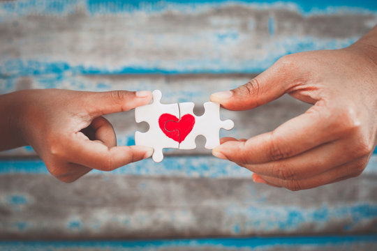 Parent and kid hands connecting couple jigsaw puzzle piece with drawn red heart