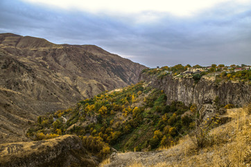 Fototapeta na wymiar The village of Garni on the basalt plateau and the slopes in the gorge, covered with autumn gardens, down to the mountain river Azat