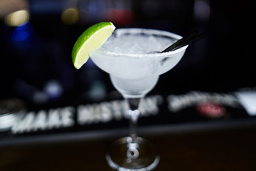 Fresh coctail on the restaurant table on dark blurred background. Blurry effect. Lime slice