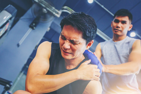 Fit man with shoulder suffering pain has treated with hot compress by his buddy after workout at fitness gym.