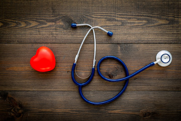 Heart health, health care concept. Stethoscope near rubber heart on dark wooden background top view