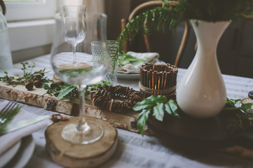 rustic festive table details with wild ferns, handmade decoration and candles. Country home dinner in summer evening.