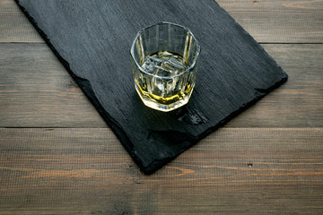 In the bar. Whiskey with ice on black desk on wooden background top view copy space