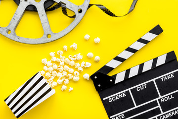 Movie premiere concept. Clapperboard, film stock, popcorn on yellow background top view