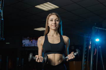 Young and beautiful woman working out with dumbbells in gym. Biceps curls.