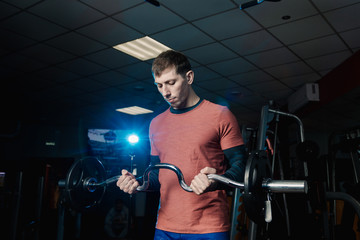 Fototapeta na wymiar Handsome athletic man trains biceps barbell in the gym.