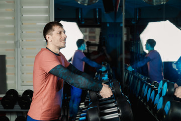 Handsome athletic man takes dumbbells from the racks for further training in the gym.