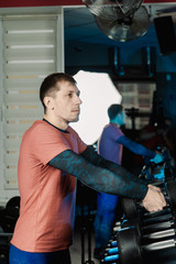 Fototapeta na wymiar Handsome athletic man takes dumbbells from the racks for further training in the gym.