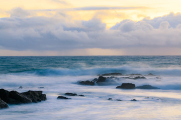 Pastel colors of sunset and silky water from long exposure of waves crashing by Pigeon Point Lighthouse on Northern California Pacific Ocean coastline at sunset