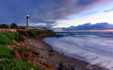 Pastel colors of sunset and silky water from long exposure of waves crashing by Pigeon Point Lighthouse on Northern California Pacific Ocean coastline at sunset