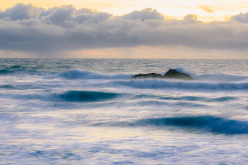 Pastel colors of sunset and silky water from long exposure of waves crashing by Pigeon Point Lighthouse on Northern California Pacific Ocean coastline at sunset