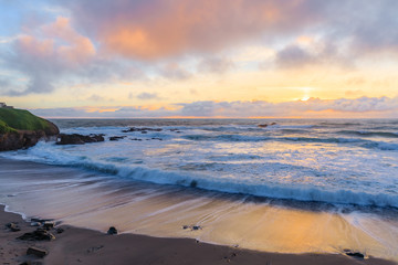 Pastel colors of sunset and silky water from long exposure of waves crashing by Pigeon Point Lighthouse on Northern California Pacific Ocean coastline at sunset