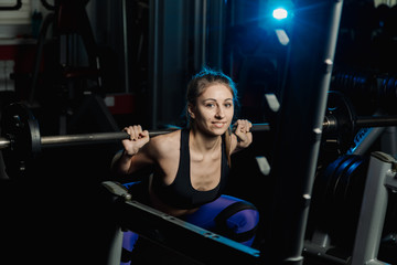 Fototapeta na wymiar Active beautiful fitness model girl crouches with a barbell on the shoulders in the gym.