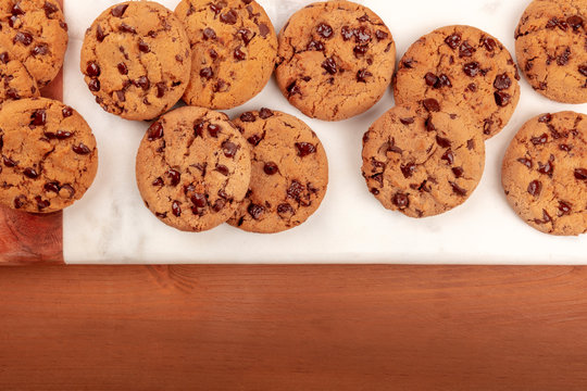 An overhead photo of freshly baked golden brown chocolate chip cookies, shot from the top on a dark rustic wooden background with copy space