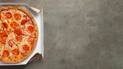 Tasty pepperoni pizza in a box on brown concrete background. Top view of hot pepperoni pizza. With...