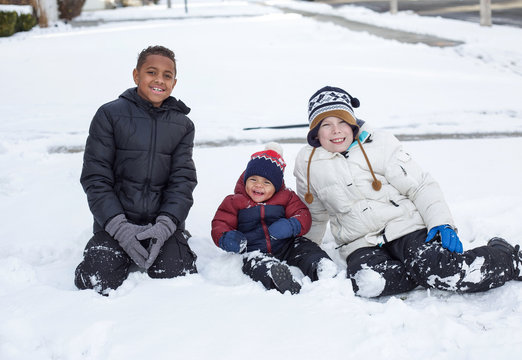 Three cute diverse boys playing together in the snow outdoors
